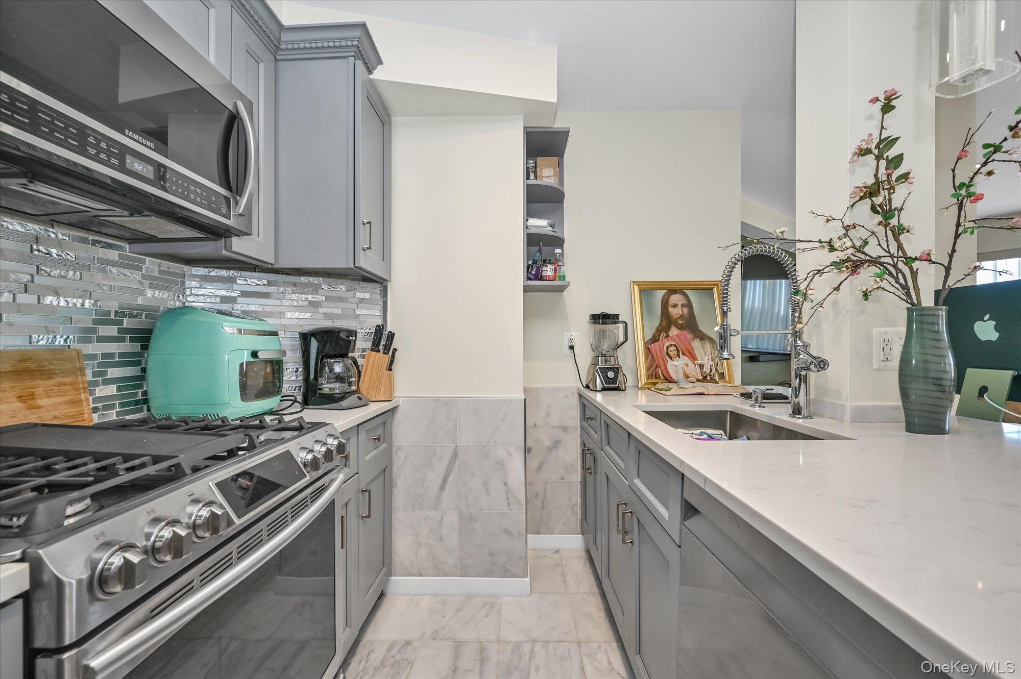 81-14 Queens Boulevard, Unit PH6C Queens, NY 11373 - Photo 6 of 19 Kitchen with gray cabinetry, appliances with stainless steel finishes, and light stone counters