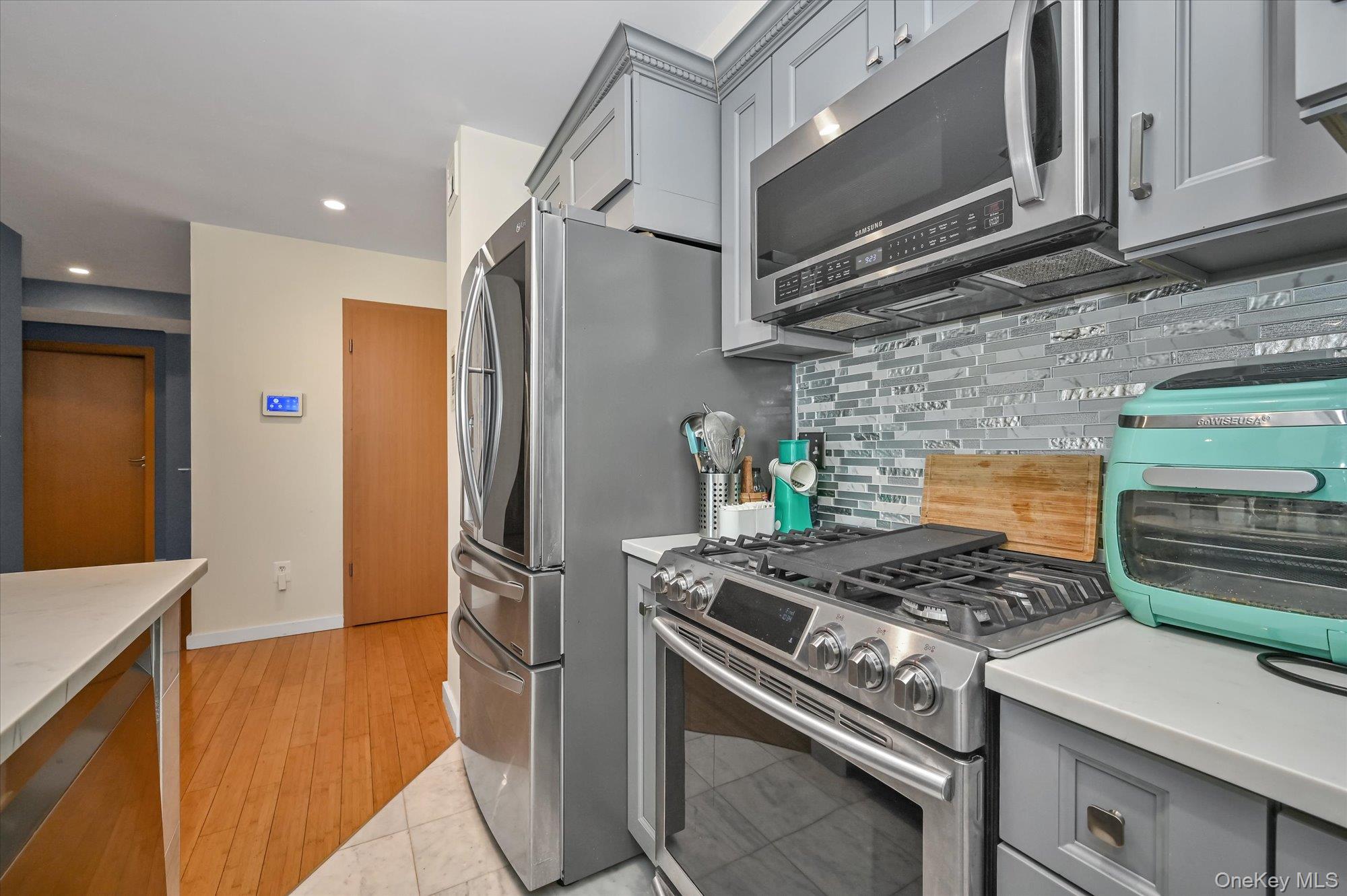 81-14 Queens Boulevard, Unit PH6C Queens, NY 11373 - Photo 7 of 19 Kitchen with gray cabinetry, appliances with stainless steel finishes, backsplash, light stone countertops, and recessed lighting