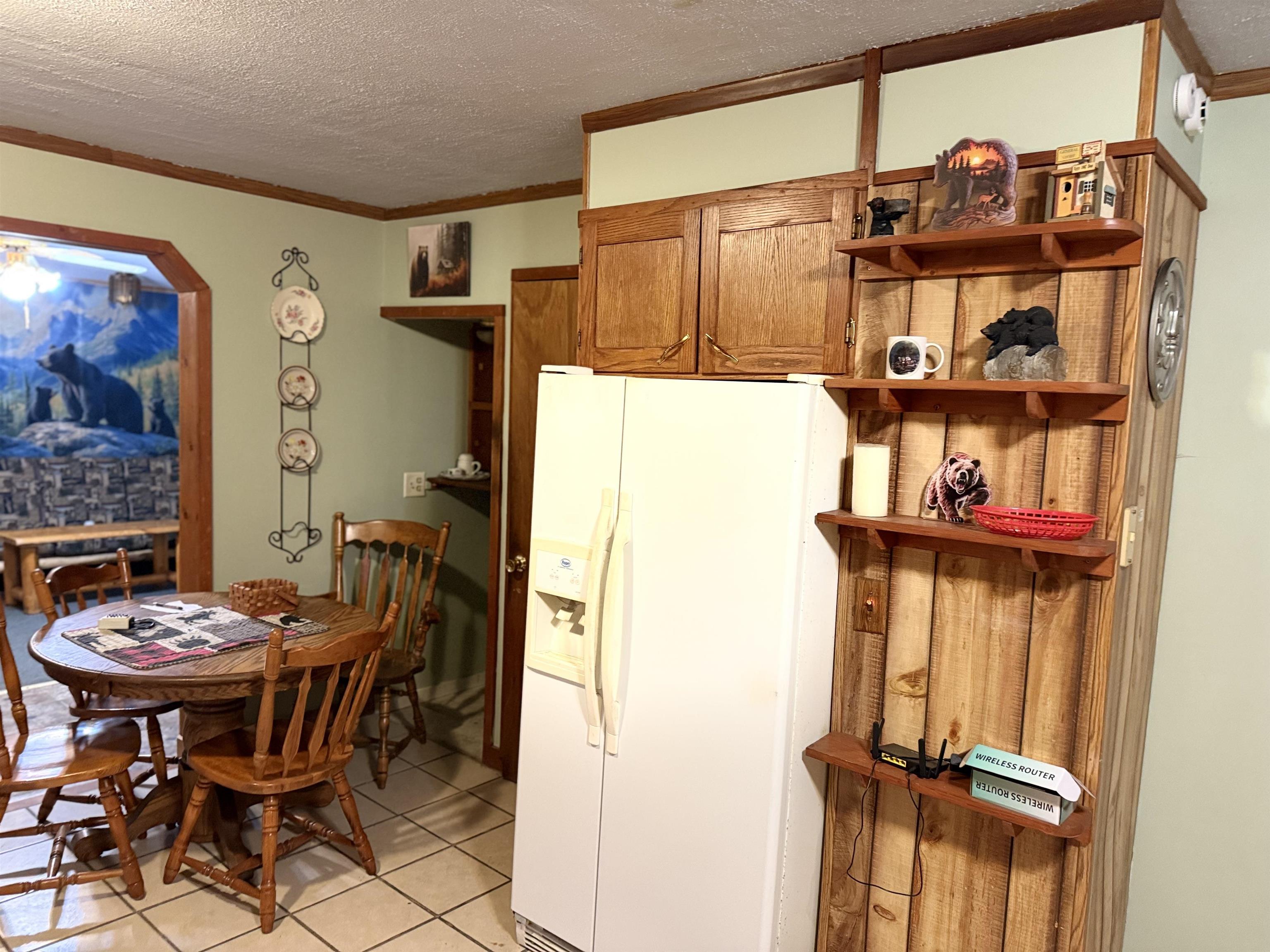 150 West 2nd Street Glidden, WI 54527 - Photo 10 of 32 Kitchen with white refrigerator with ice dispenser, brown cabinetry, a textured ceiling, crown molding, and light tile patterned floors