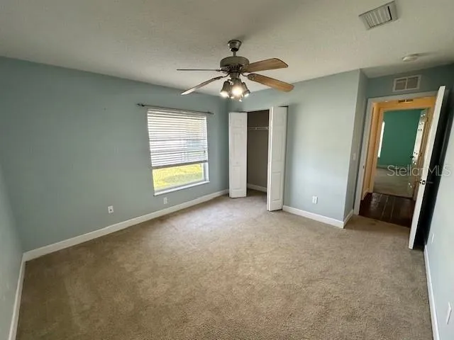 an empty room with chandelier fan and windows