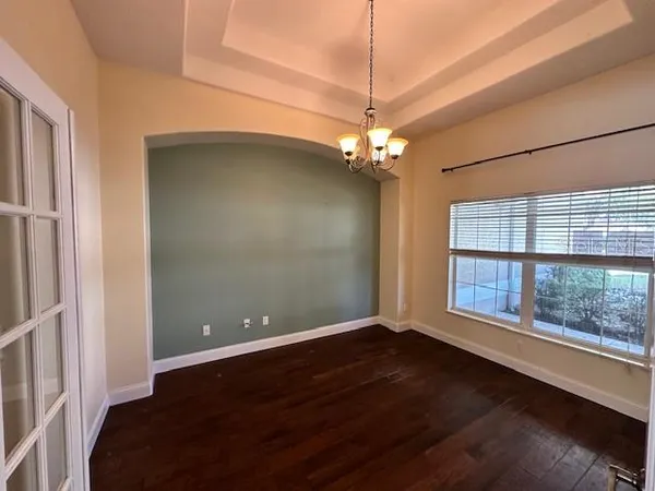 an empty room with wooden floor chandelier and windows