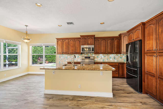 20933 La Plata Court Boca Raton, FL 33428 - Photo 12 of 60 a kitchen with stainless steel appliances granite countertop a refrigerator a stove top oven a sink dishwasher and wooden cabinets with wooden floor
