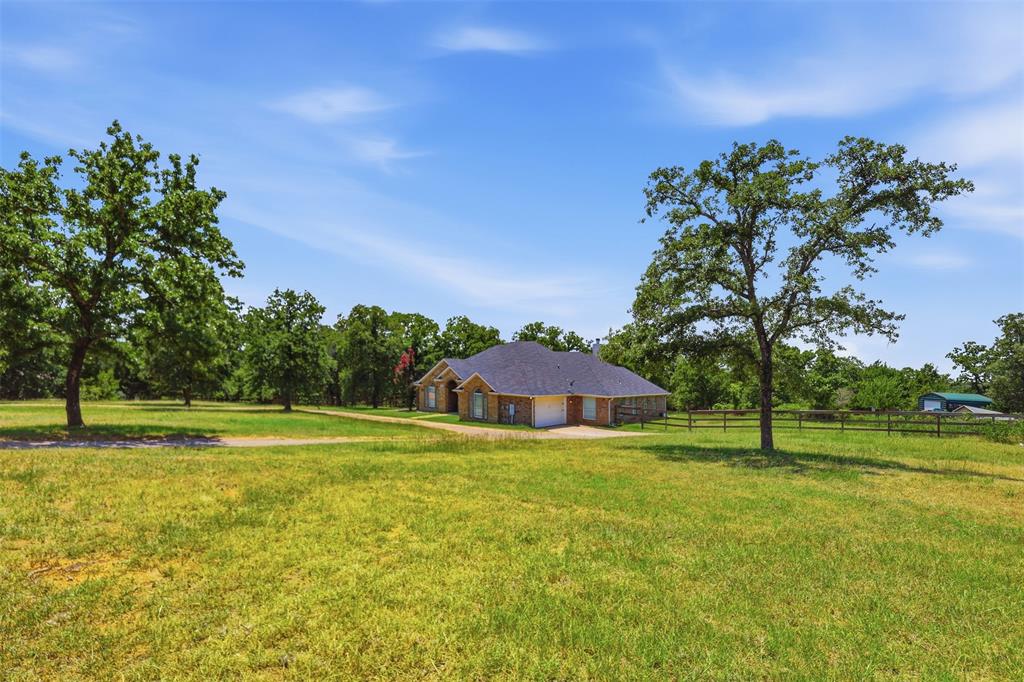 4417 Slayton Road Cleburne, TX 76031 - Photo 11 of 28 Expansive grass lawn surrounding a single-story brick residence with a dark shingle roof and a two-car garage