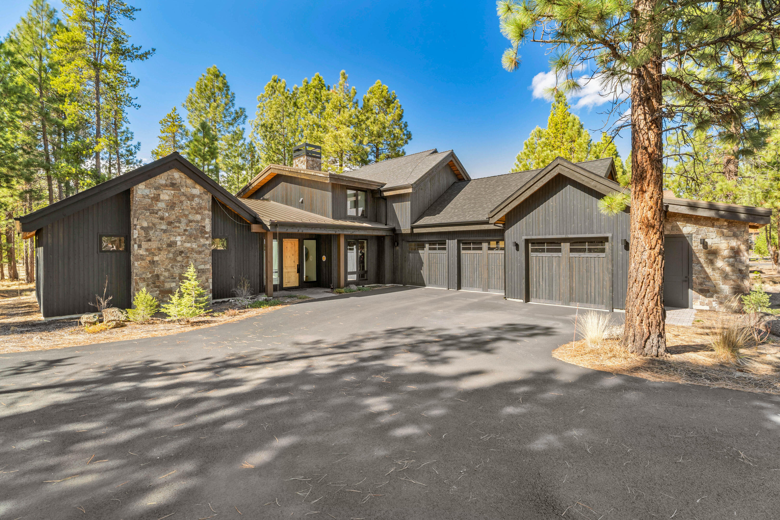 56670 Sunstone Loop, Unit LOT 141 Bend, OR 97707 - Photo 9 of 62 Designed by Wright Design Studio and built by Olsen Brothers Construction, this front elevation showcases clean mountain modern lines, stained cedar siding, substantial stonework, and warm natural materials. The private corner setting and level .41-acre lot enhance both curb appeal and livability.