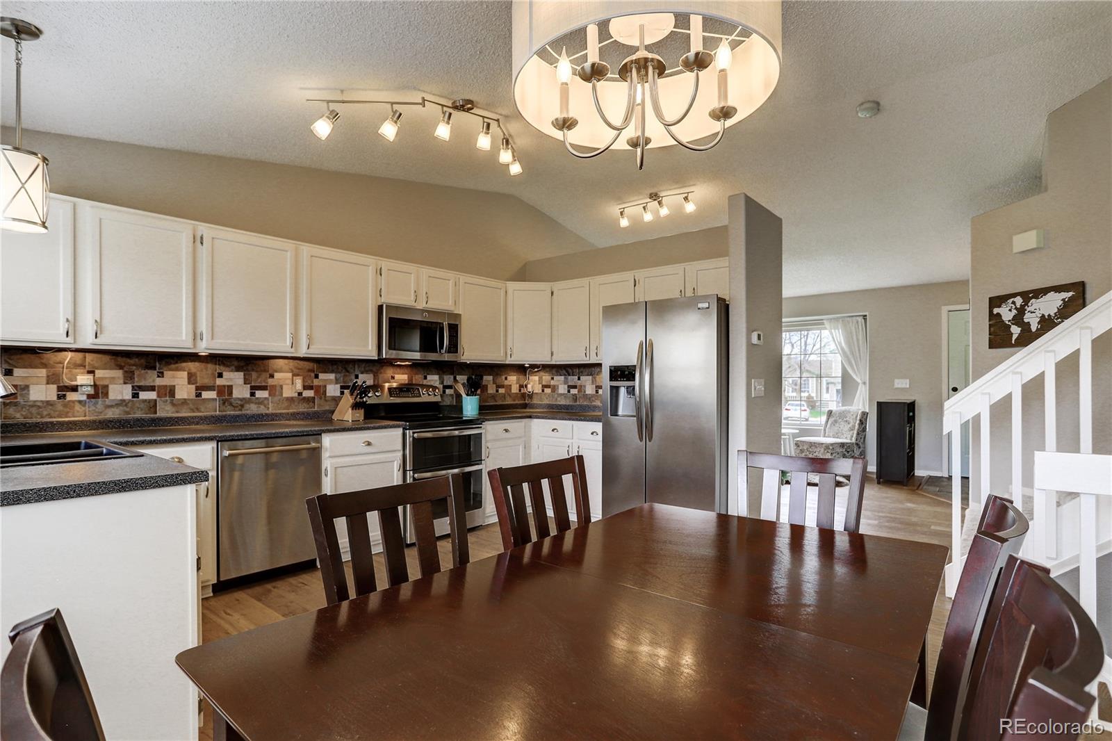 10626 Hyacinth Court Highlands Ranch, CO 80129 - Photo 9 of 38 a kitchen with stainless steel appliances granite countertop a dining table chairs wooden floor and a refrigerator