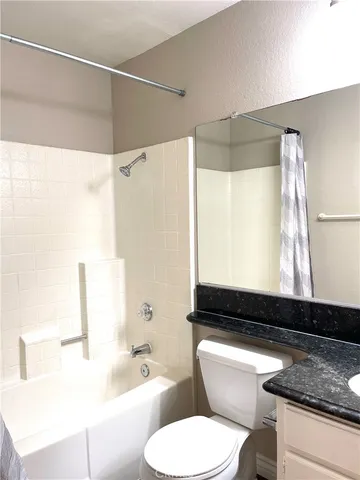 a bathroom with a granite countertop bathtub sink vanity mirror and toilet