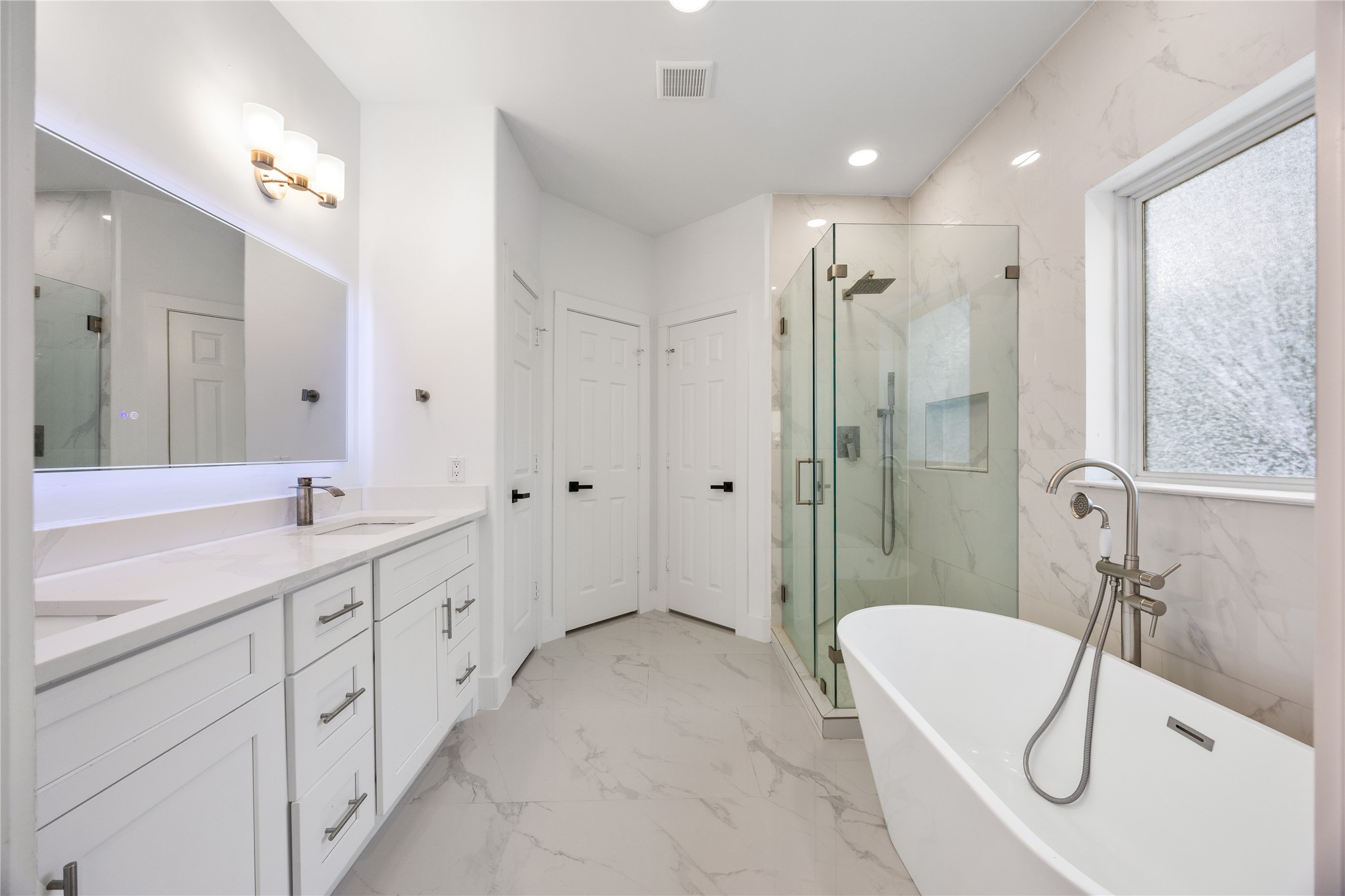 1121 Austin Street Rosenberg, TX 77471 - Photo 27 of 44 This modern bathroom features a sleek design with a freestanding tub, glass-enclosed shower, dual sinks with ample cabinetry, and elegant fixtures. The space is bright and airy, enhanced by a large window and stylish quartz accents.