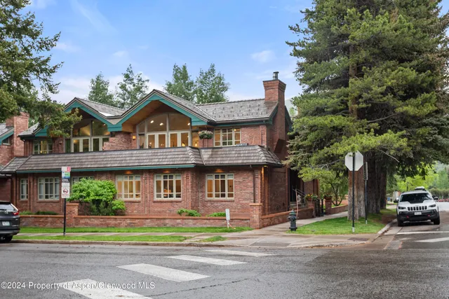 a view of a brick house with a large windows and a big yard and large trees