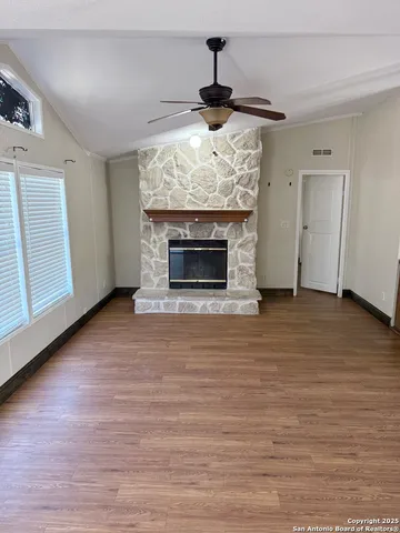 a view of an empty room with wooden floor fireplace and a window