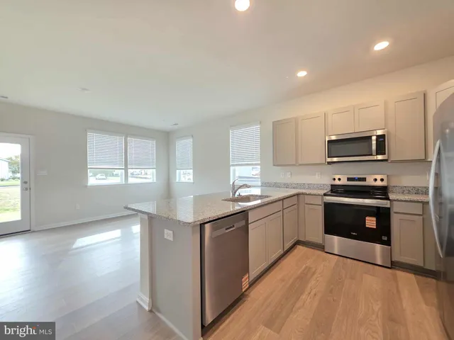 a kitchen with stainless steel appliances granite countertop a stove top oven a sink dishwasher and a refrigerator with wooden floor