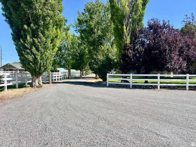 812 East Bates Cyn Road Tooele, UT 84074 - Photo 104 of 144 Gravel driveway bordered by white fencing, mature deciduous trees, and manicured green lawn