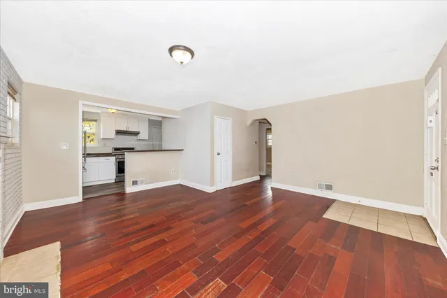 a view of empty room with wooden floor and kitchen