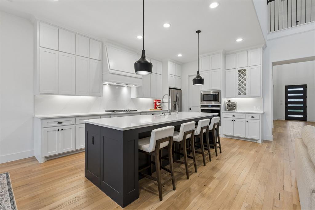 566 Broadleaf Way Haslet, TX 76052 - Photo 14 of 38 Gourmet kitchen featuring a large central island with seating, extensive white cabinetry, light-toned wood-finish flooring, recessed lighting, and modern pendant fixtures