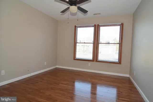 an empty room with wooden floor chandelier fan and windows