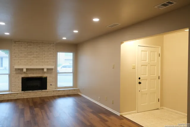 an empty room with wooden floor fireplace and windows