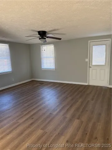 an empty room with wooden floor ceiling fan and windows