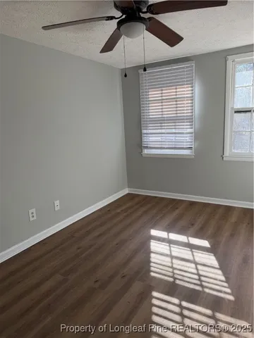an empty room with wooden floor fan and windows