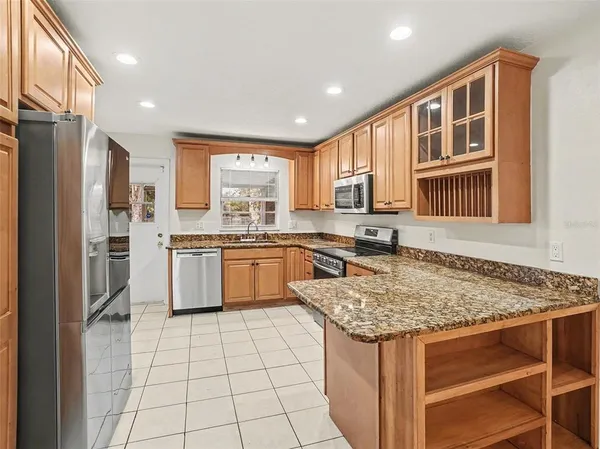 a kitchen with stainless steel appliances granite countertop a stove a sink dishwasher a refrigerator and white cabinets with wooden floor