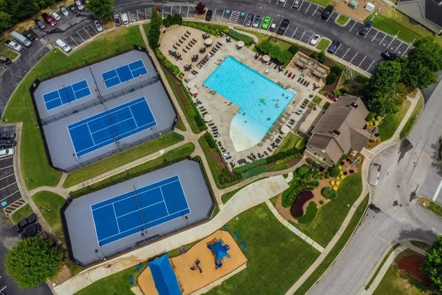 an aerial view of a tennis ground and a cars park side of the road
