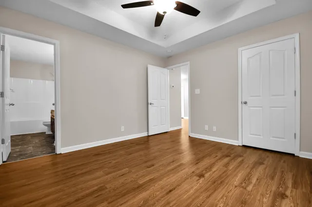 a view of an empty room with wooden floor and a ceiling fan