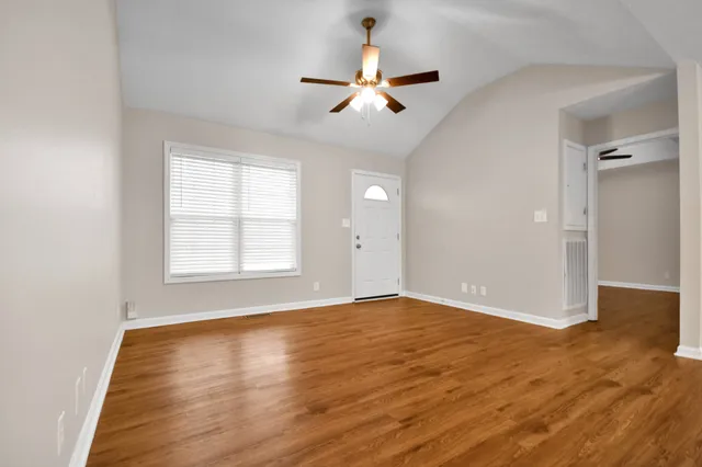 an empty room with wooden floor chandelier fan and windows