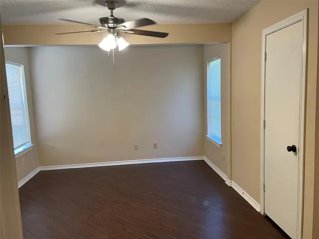 an empty room with wooden floor fan and windows