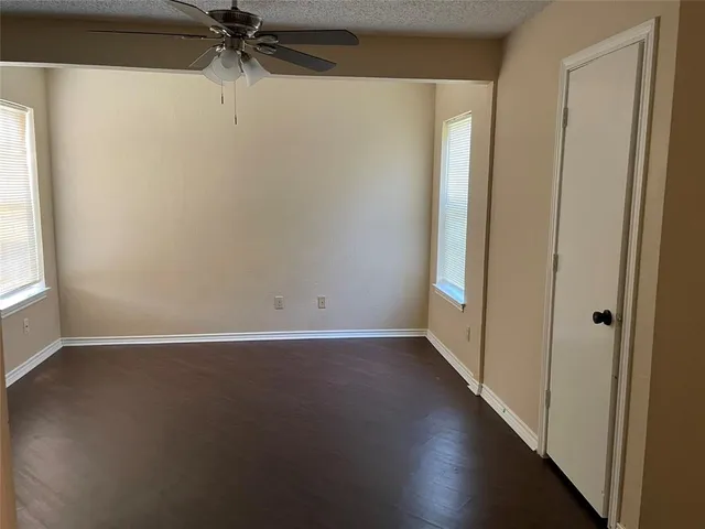 an empty room with wooden floor fan and windows