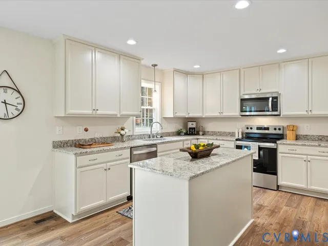 a kitchen with stainless steel appliances granite countertop a stove top oven a sink a refrigerator and white cabinets with wooden floor