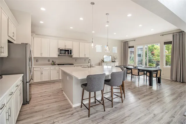 a kitchen with stainless steel appliances granite countertop a stove top oven a sink dishwasher a dining table and chairs with wooden floor