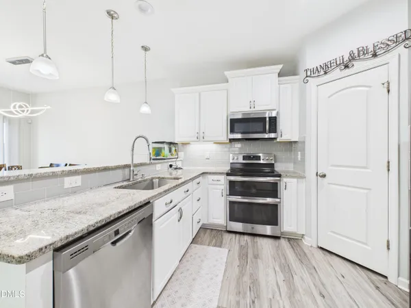 a kitchen with stainless steel appliances kitchen island granite countertop a stove a sink and white cabinets with wooden floor