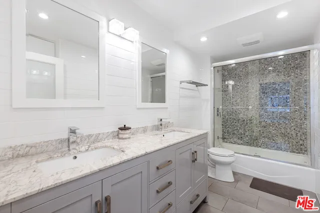 a bathroom with a granite countertop sink a toilet a mirror a bathtub and shower