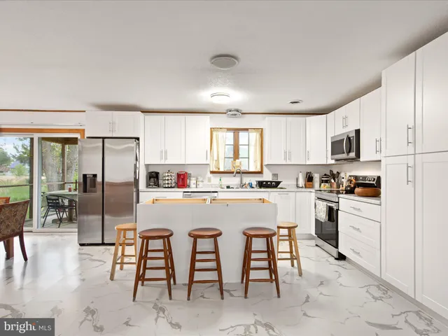 a kitchen with stainless steel appliances granite countertop a stove a sink a refrigerator and white cabinets with wooden floor