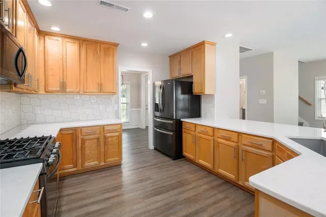 a large kitchen with stainless steel appliances granite countertop a stove a sink dishwasher and a refrigerator with wooden floor