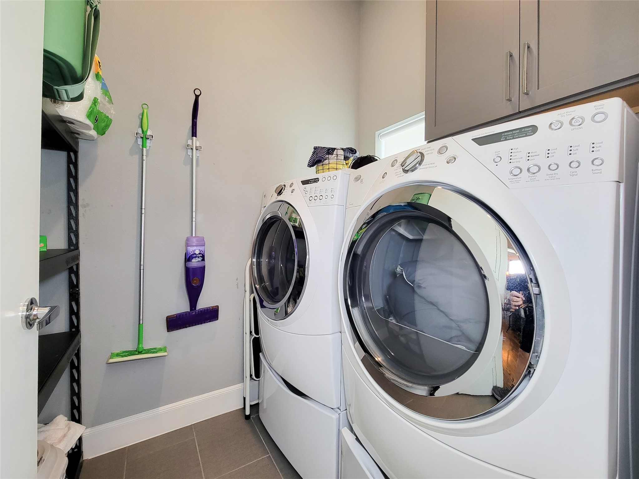 1705 Eado Point Lane Houston, TX 77003 - Photo 32 of 50 Laundry room with front-loading washer and dryer, shelving for storage, and a space for cleaning supplies neatly organized on the wall.