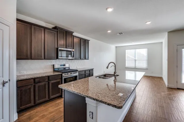 a kitchen with stainless steel appliances granite countertop a sink dishwasher stove and refrigerator with wooden floor
