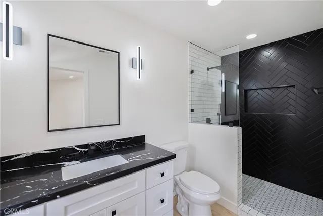 a bathroom with a granite countertop sink a toilet a mirror and shower