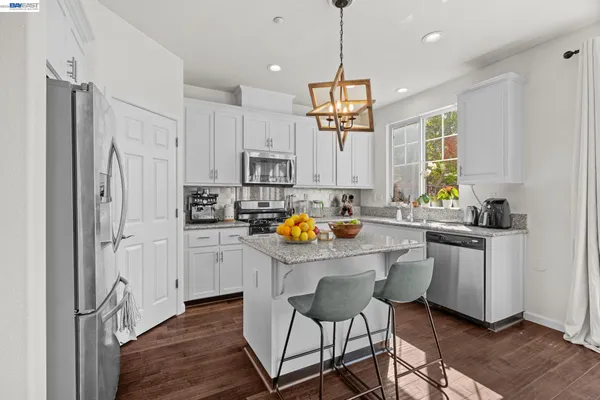 a kitchen with stainless steel appliances a refrigerator a stove a sink and white cabinets with wooden floor