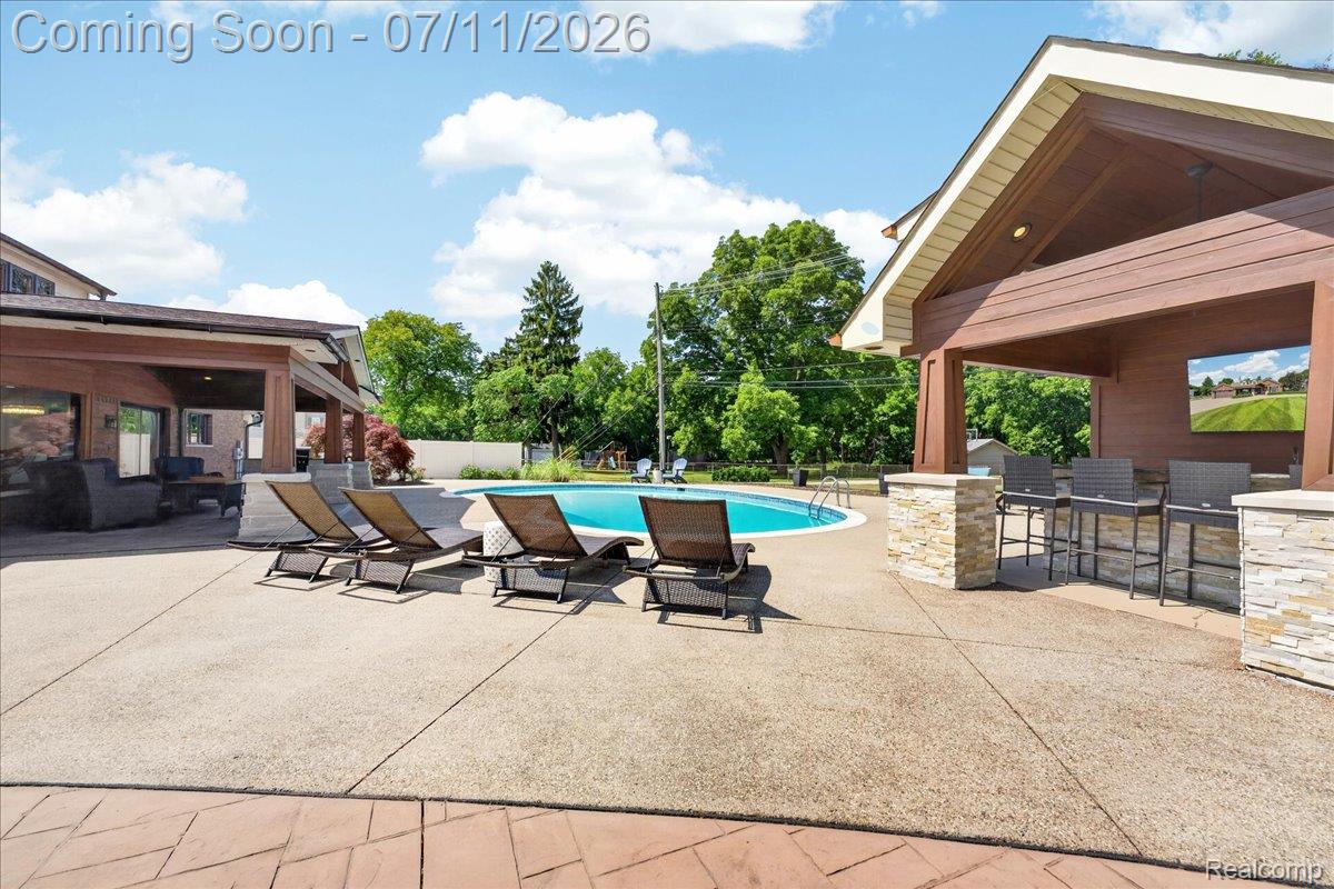 23750 East River Road Grosse Ile, MI 48138 - Photo 38 of 54 Outdoor oasis featuring a circular swimming pool, an expansive concrete patio, and a covered lounge area with a stone-clad bar