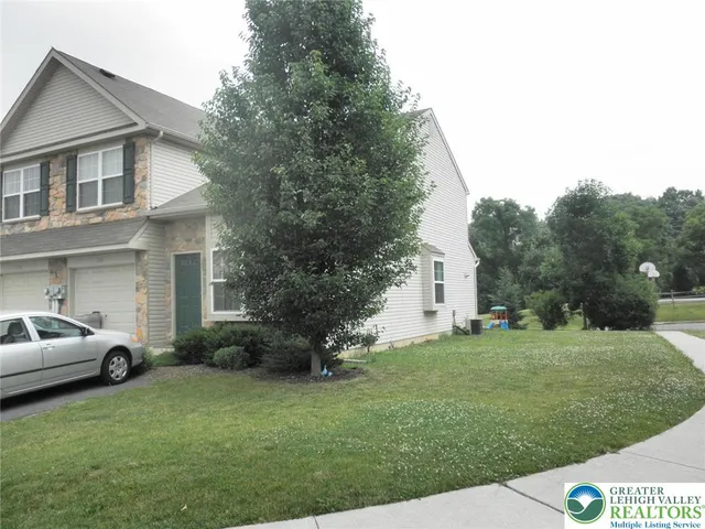 a view of a white house in front of a big yard with plants and large trees