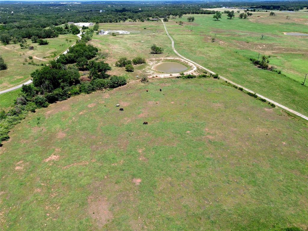 2186 Gilliland Road Springtown, TX 76082 - Photo 25 of 25 Expansive agricultural land featuring a natural pond, a dirt track, and scattered mature trees