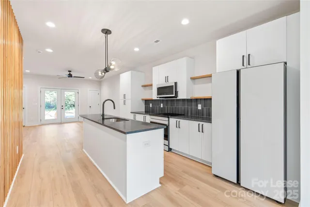 a kitchen with granite countertop a refrigerator a sink a stove and white cabinets with wooden floor