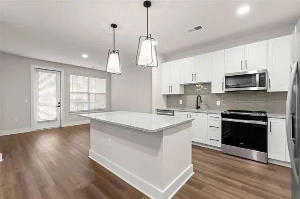 a kitchen with stainless steel appliances granite countertop a stove a sink dishwasher a refrigerator white cabinets and wooden floor