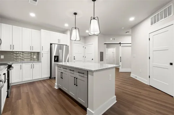 a large kitchen with stainless steel appliances kitchen island granite countertop a refrigerator a sink dishwasher a stove and white cabinets with wooden floor