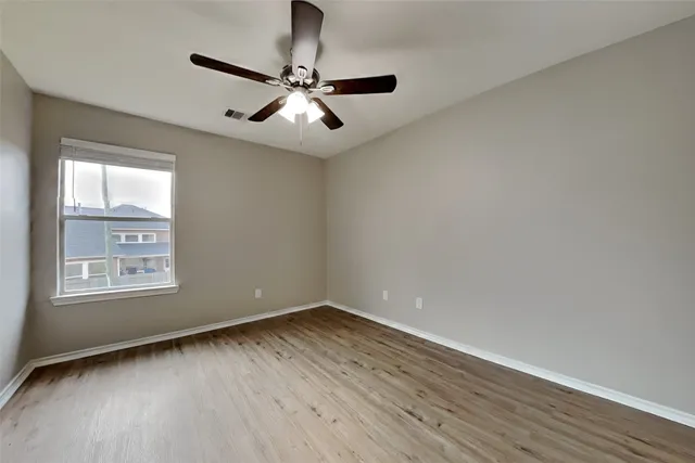 an empty room with wooden floor chandelier fan and windows