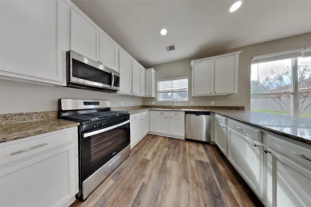 a kitchen with stainless steel appliances granite countertop wooden cabinets a stove a sink and a microwave