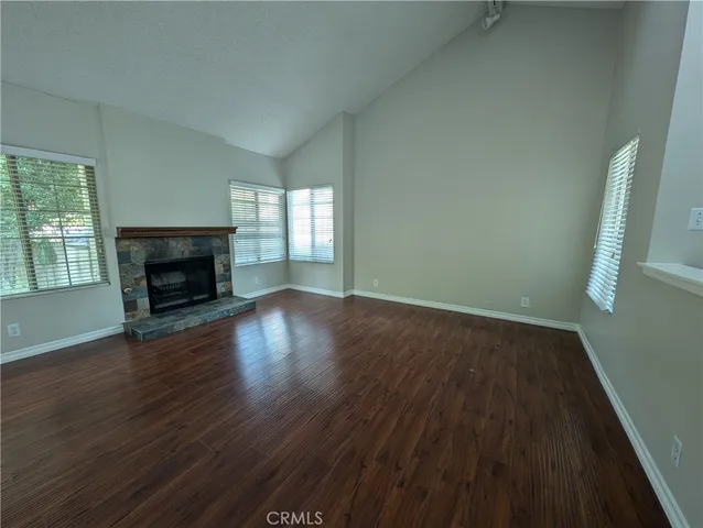 an empty room with wooden floor fireplace and windows