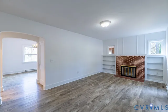 an empty room with wooden floor fireplace and windows