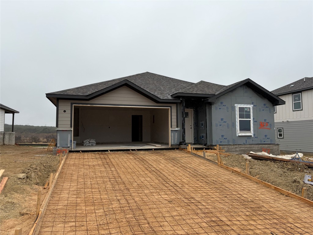 View of front facade with a shingled roof, decorative driveway, and an attached garage