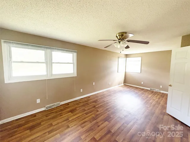 an empty room with wooden floor fan and windows