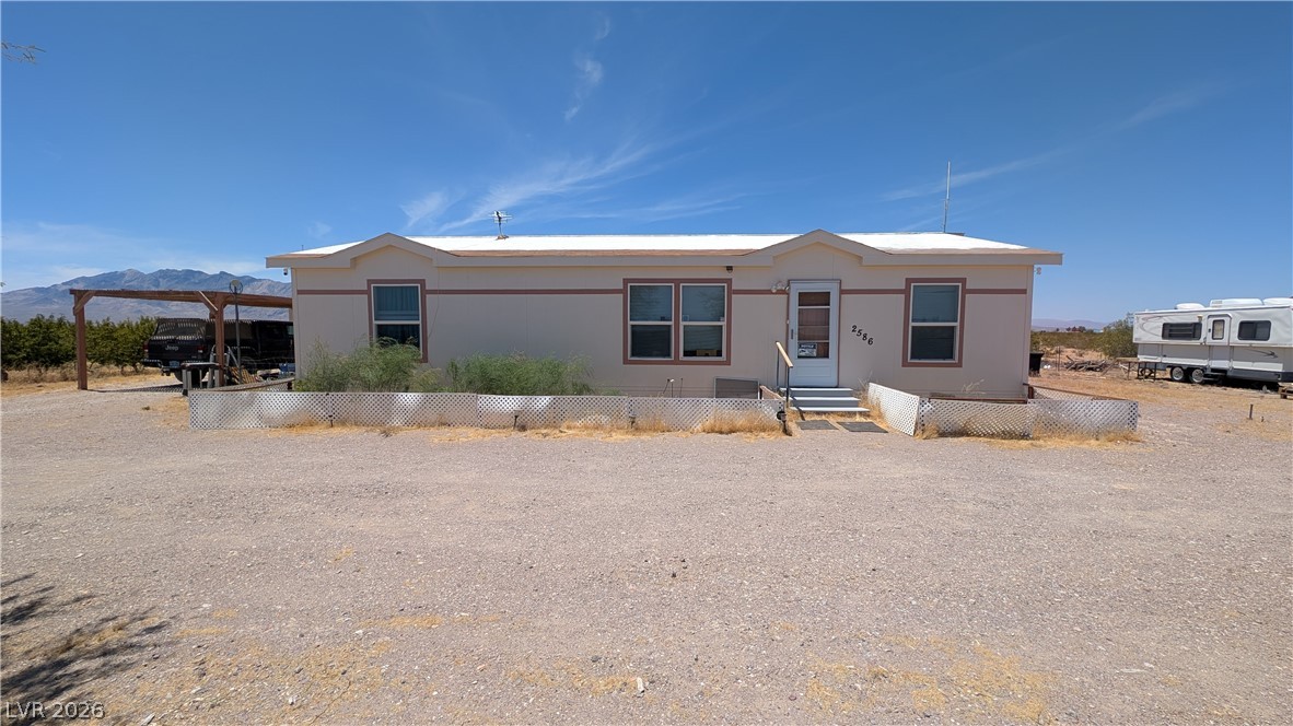 2586 South Miner Road Amargosa Valley, NV 89020 - Photo 1 of 10 A desert-landscape home features a carport and open gravel area.